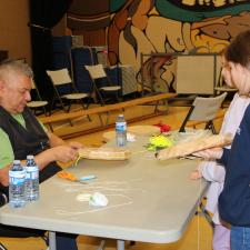 Knowledge Keeper Darren Charlie helps two grade 5 female students with their drums